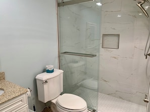A bathroom with a toilet, a shower enclosure, and a marble-tiled wall. - 858 Ketch Court at The Sea Pines Resort (Hilton Head Island)