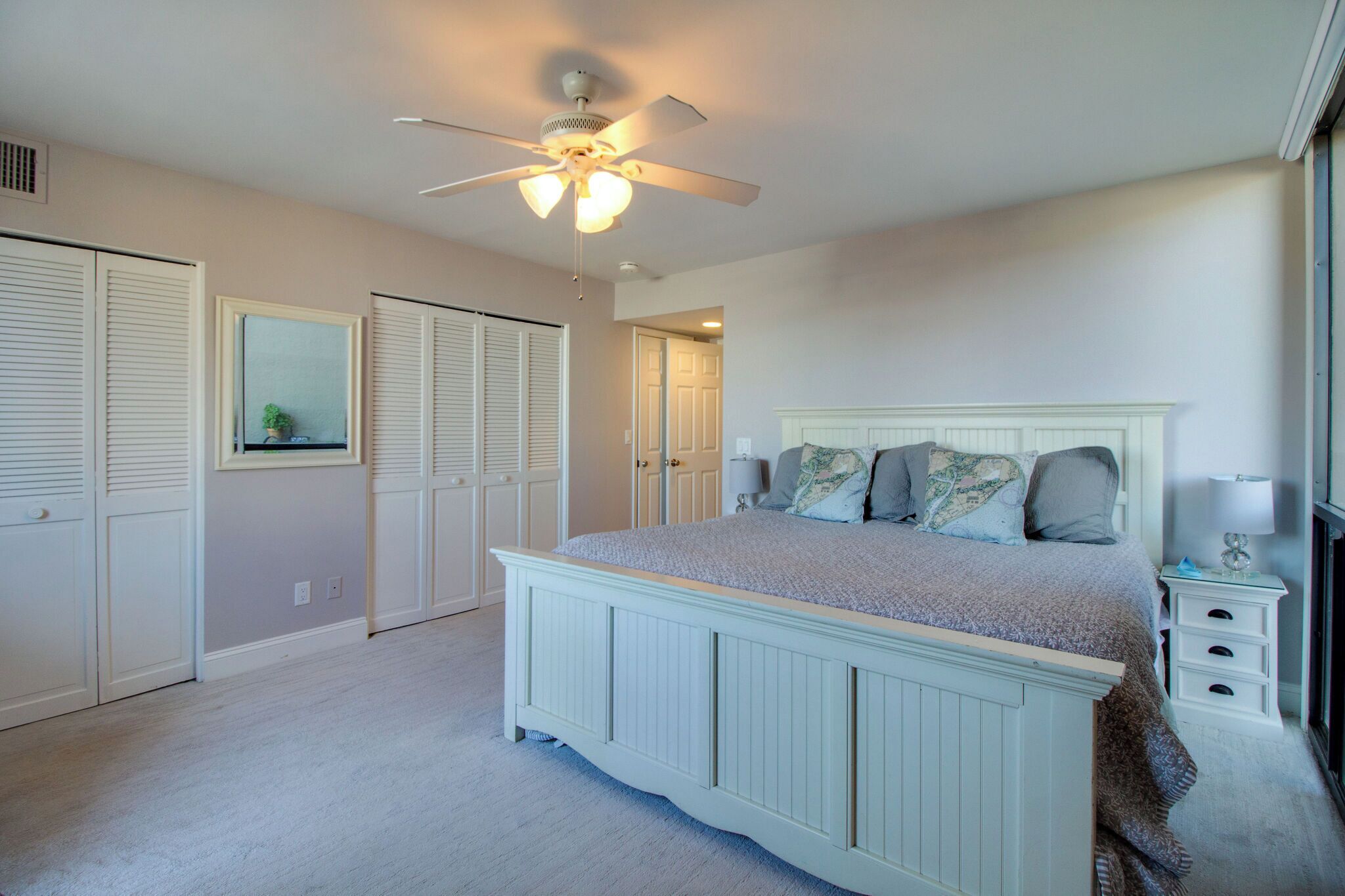 A bedroom with a large bed, a ceiling fan, and a window with blinds.