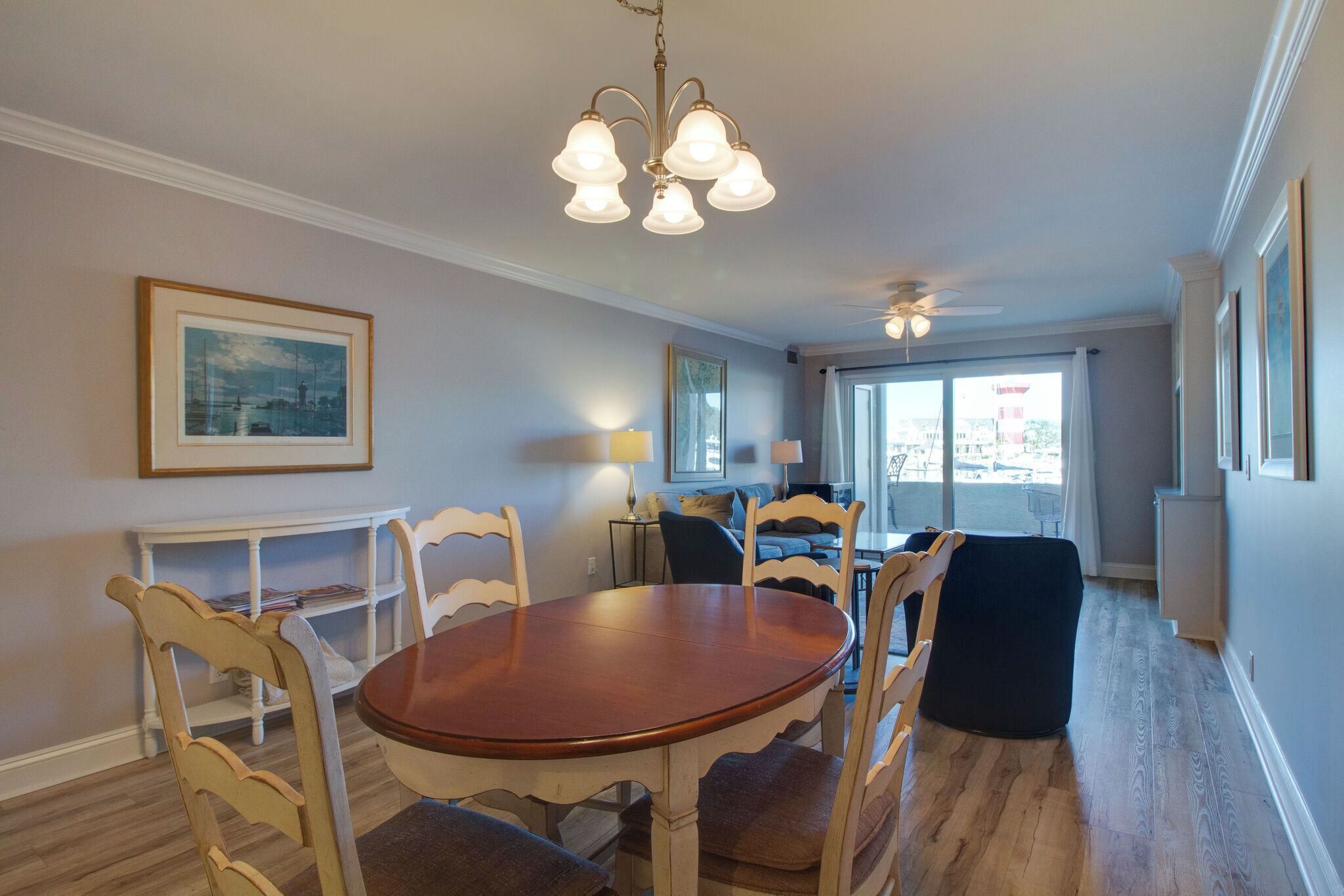 A dining area with a wooden table and chairs, a chandelier, and a view of the city through large windows.