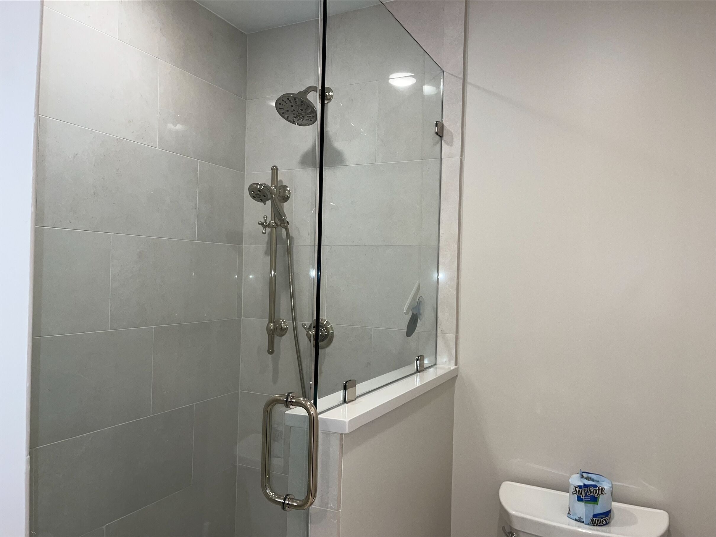 Un baño moderno con ducha de vidrio, lavamanos blanco y retrete.