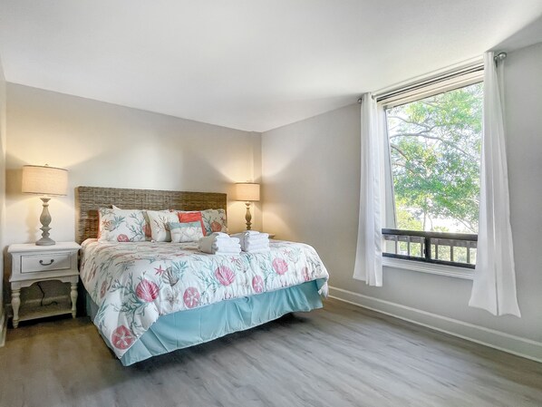 A bedroom with a bed, two bedside tables, a window with curtains, and a view of trees outside. - 926 Cutter Court at The Sea Pines Resort (Hilton Head Island)