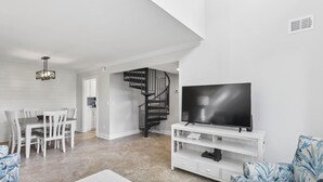 Un saló modern amb televisió plana, mobiliari blanc, una escala i una zona de menjador.