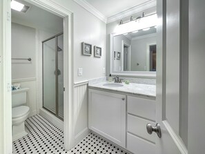 Un baño con inodoro blanco, ducha con puerta de vidrio, lavamanos con espejo superior y suelo estampado.