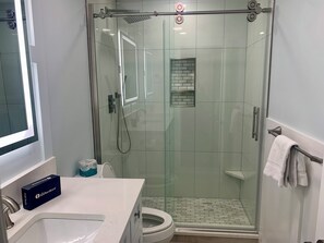 Un baño moderno con ducha envuelta en vidrio, inodoro y lavamanos con toallero.