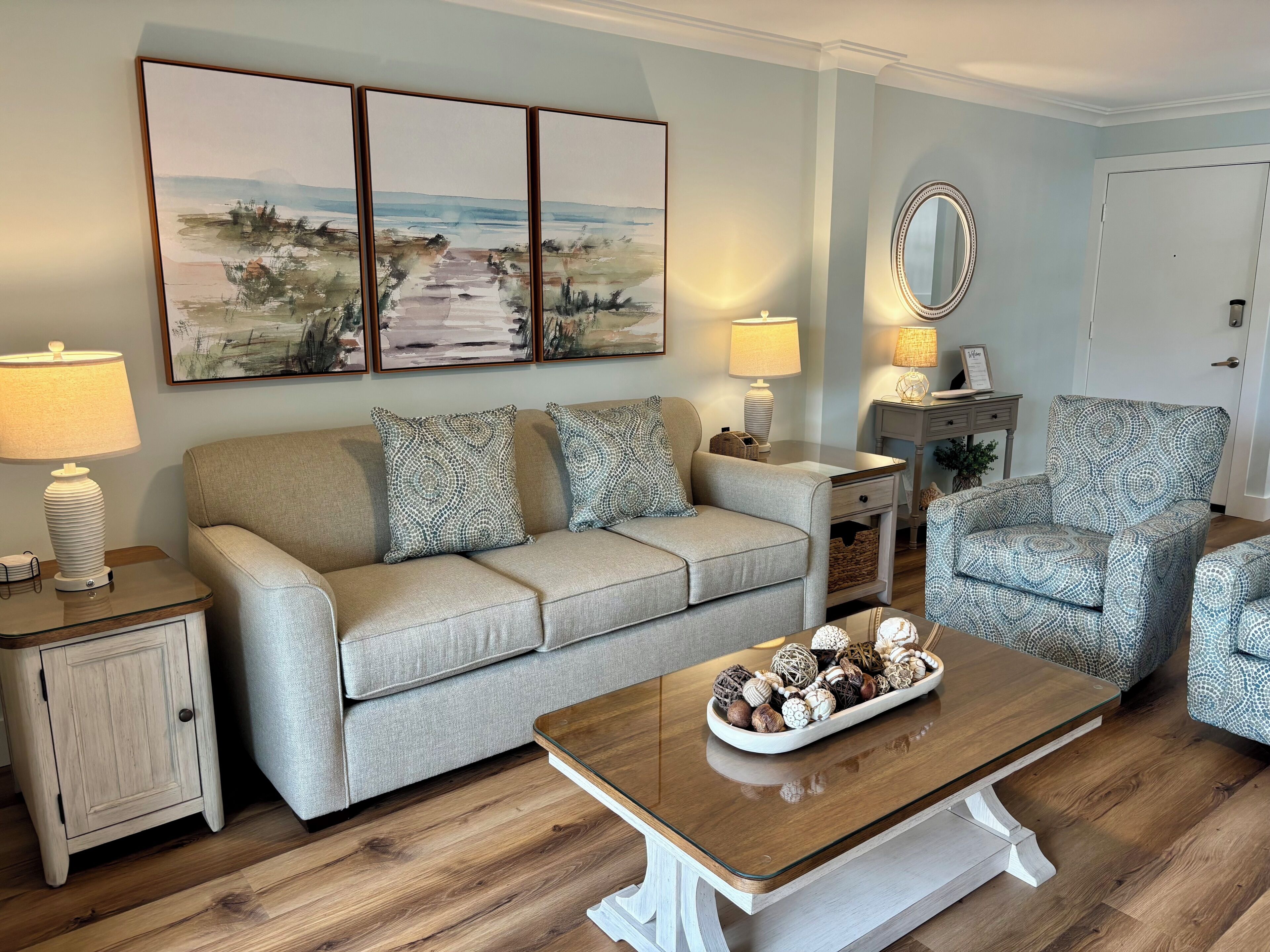 A living room with a sofa, armchair, coffee table, lamps, and a painting on the wall.