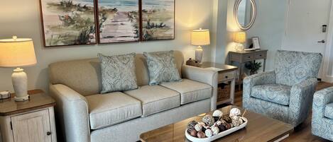 A living room with a sofa, armchair, coffee table, lamps, and a painting on the wall.