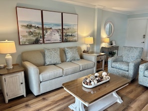 A living room with a sofa, armchair, coffee table, lamps, and a painting on the wall. - 884 Ketch Court at The Sea Pines Resort (Hilton Head Island)