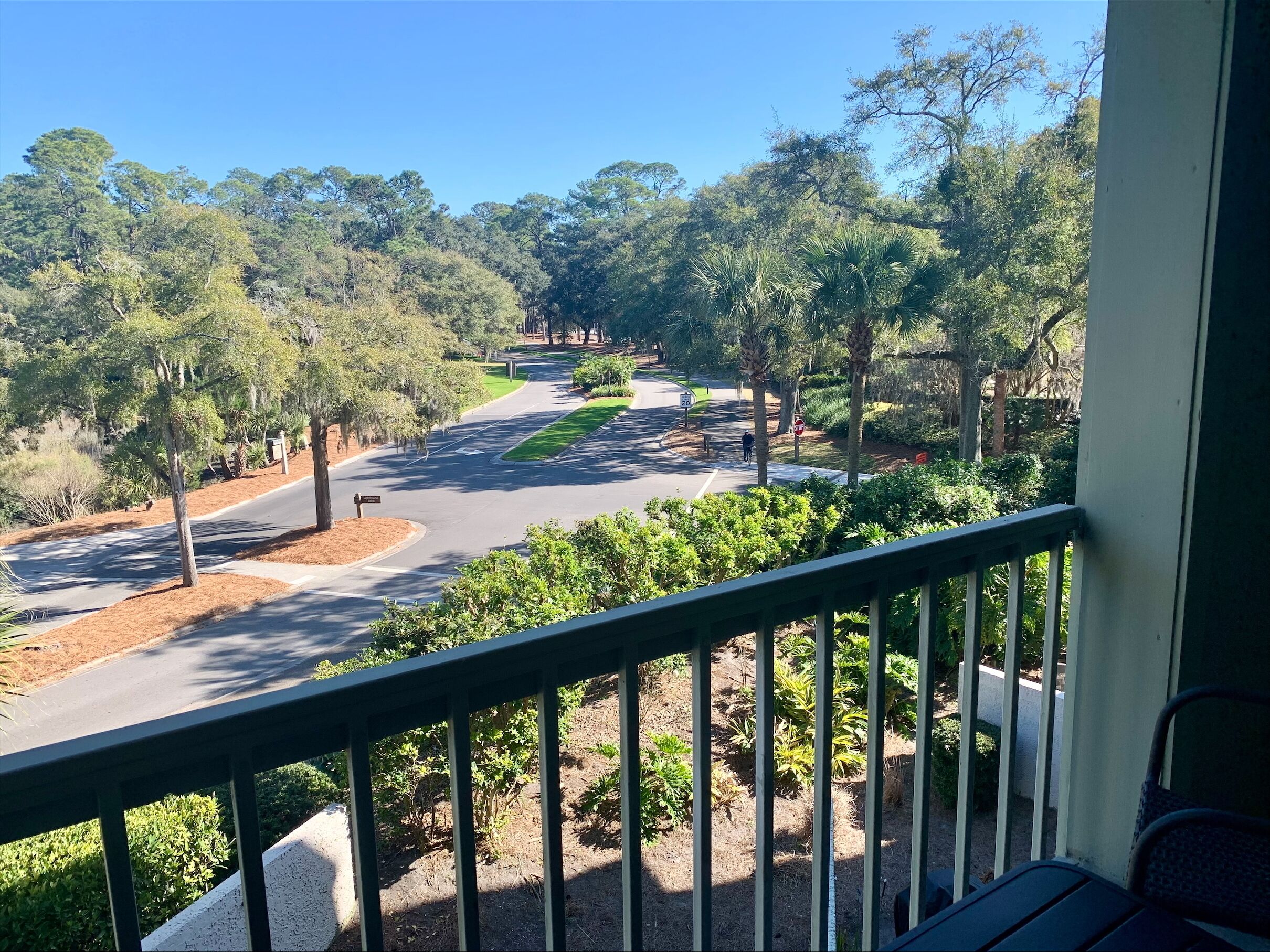 A balcony with a view of a road curving through a landscaped area with trees and shrubs.