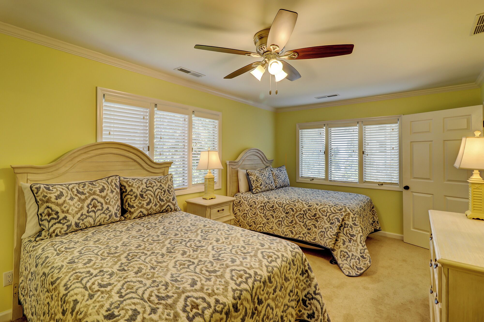 A bedroom with two beds, a ceiling fan, and a door.