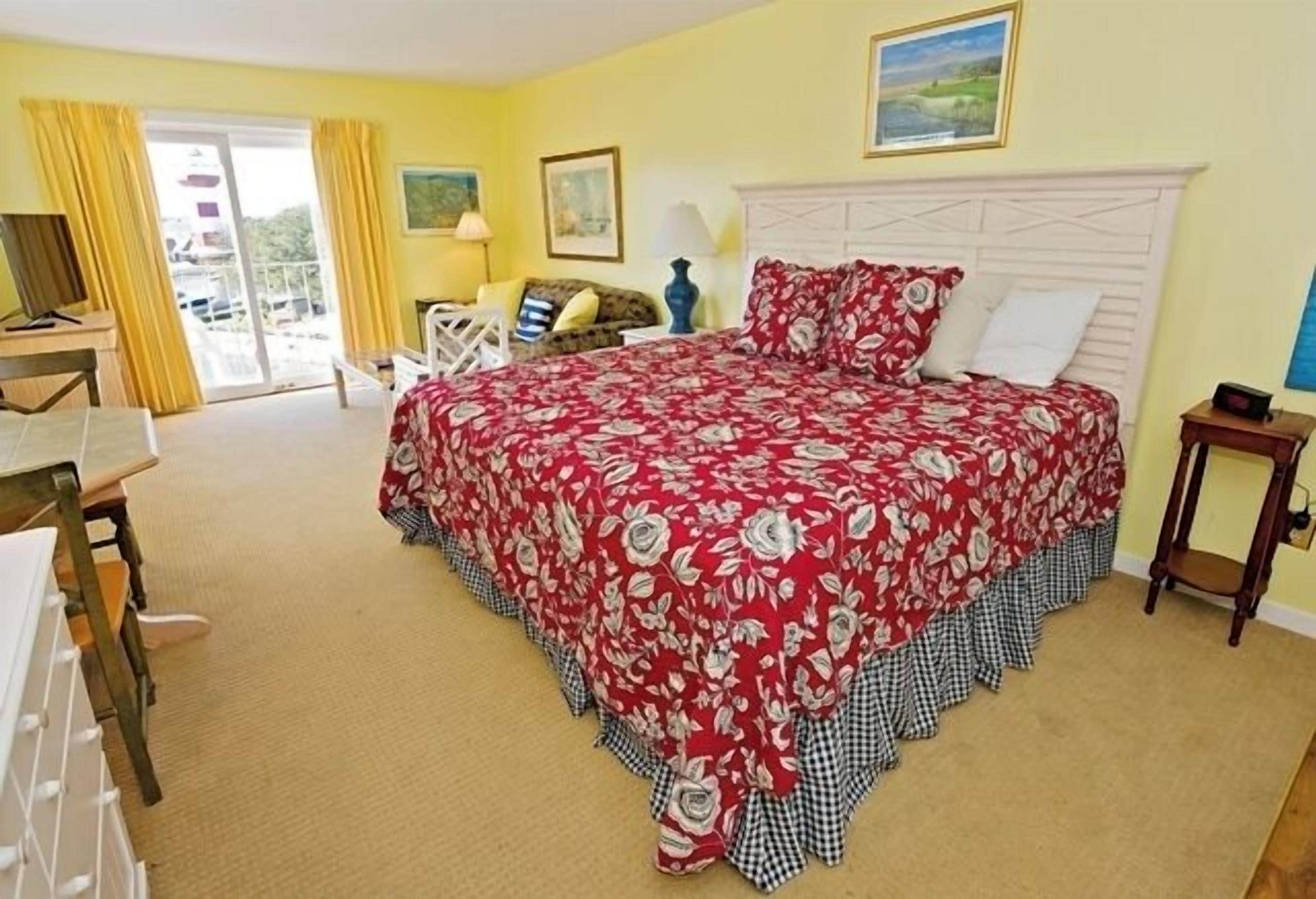 A bedroom with a large bed, a desk, a chair, and a view of the outdoors.