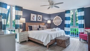 Une chambre à coucher comprenant un lit, des tables de chevet, un ventilateur de plafond et une fenêtre avec des rideaux.