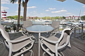 Eine Terrasse mit einem runden Tisch und vier Stühlen mit Blick auf einen Yachthafen, wo Boote und ein Leuchtturm liegen.