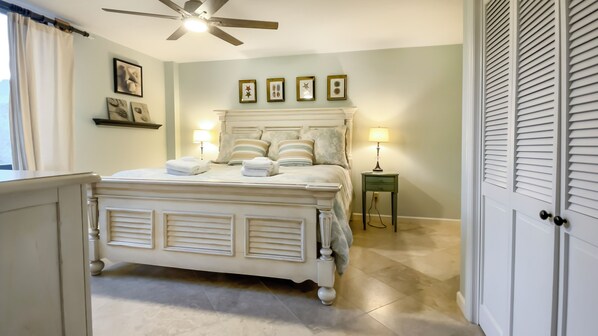 Quarto com cama, luminárias de cabeceira, ventilador de teto e quadros nas paredes.