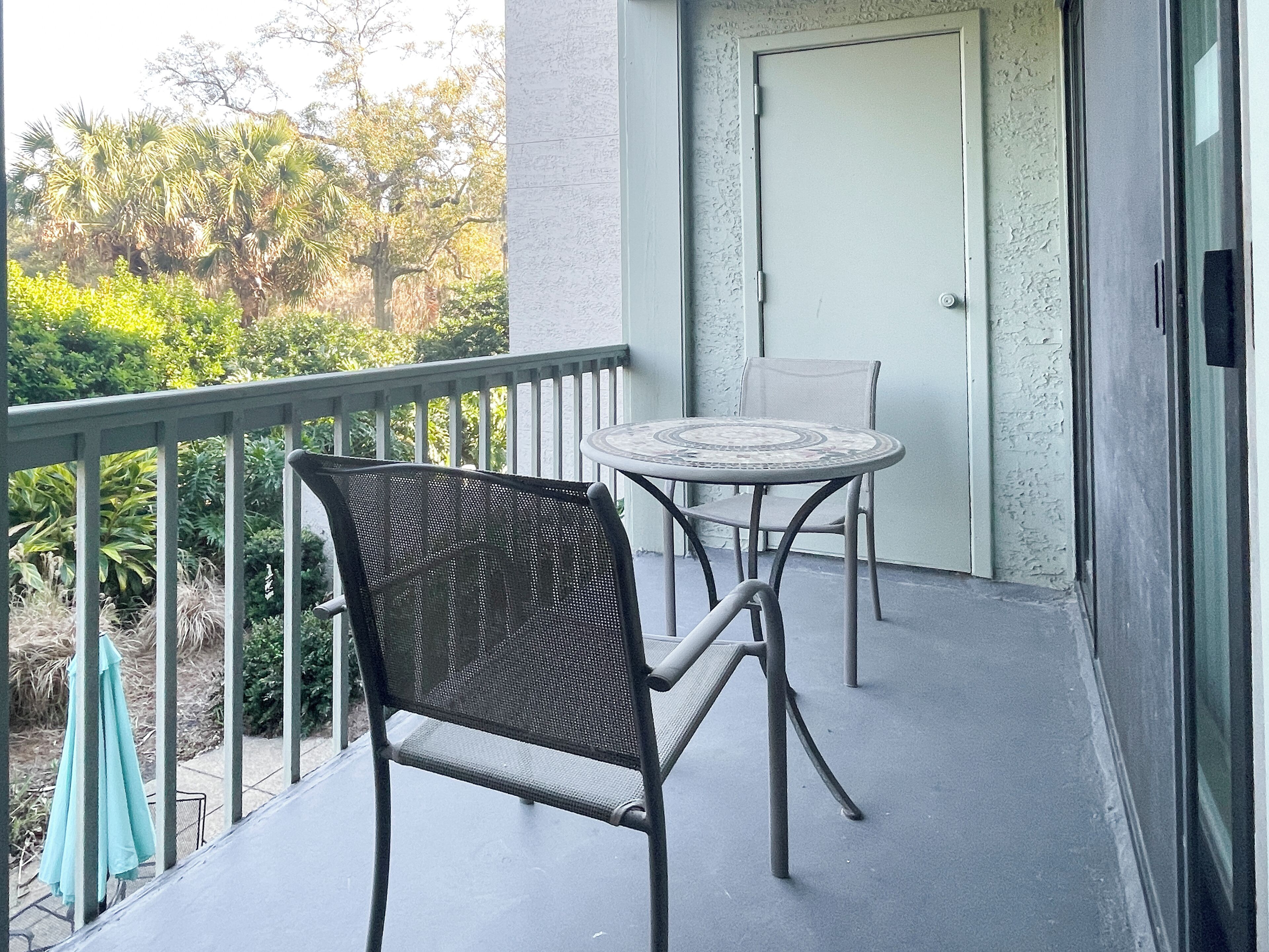Un balcon avec une table et des chaises, une porte et une vue sur la verdure.