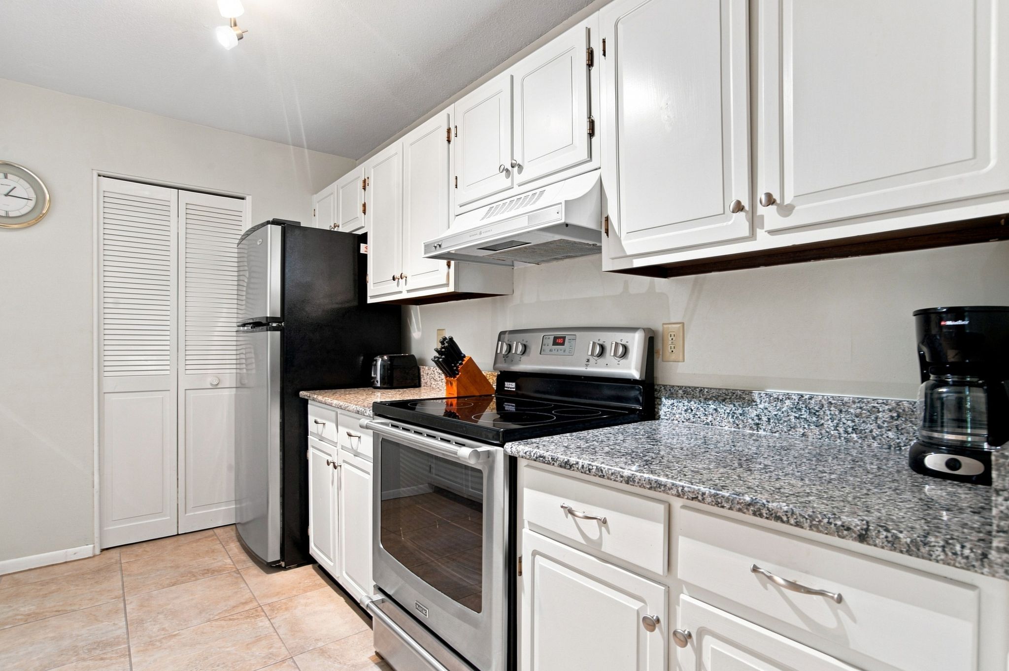 A kitchen with white cabinets, a black refrigerator, a stove, and a coffee maker.