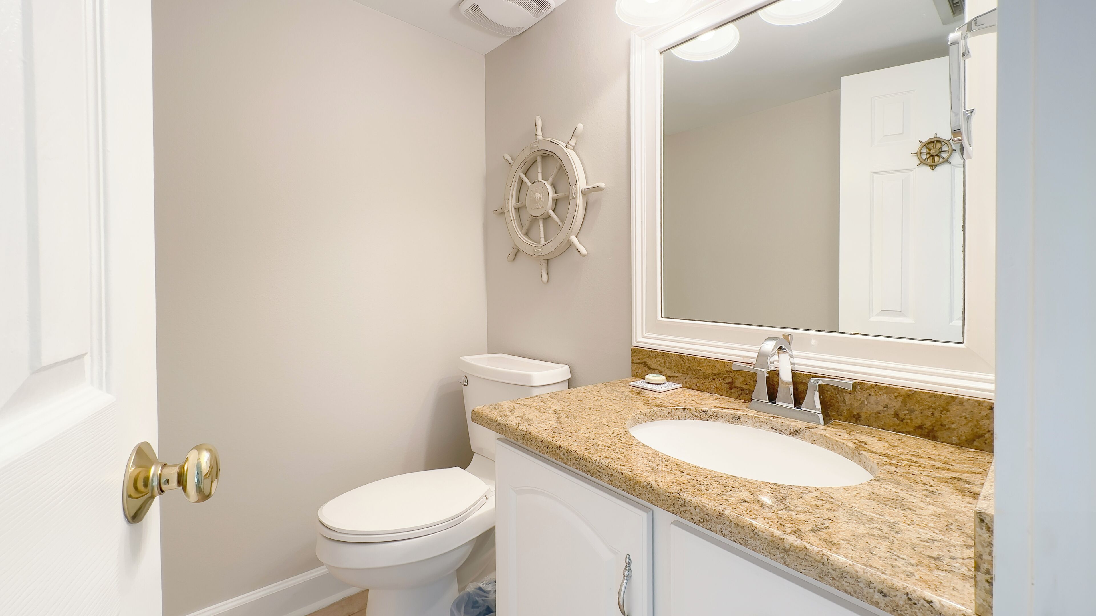 Un baño con inodoro, lavabo y una decoración de timón de barco en la pared.