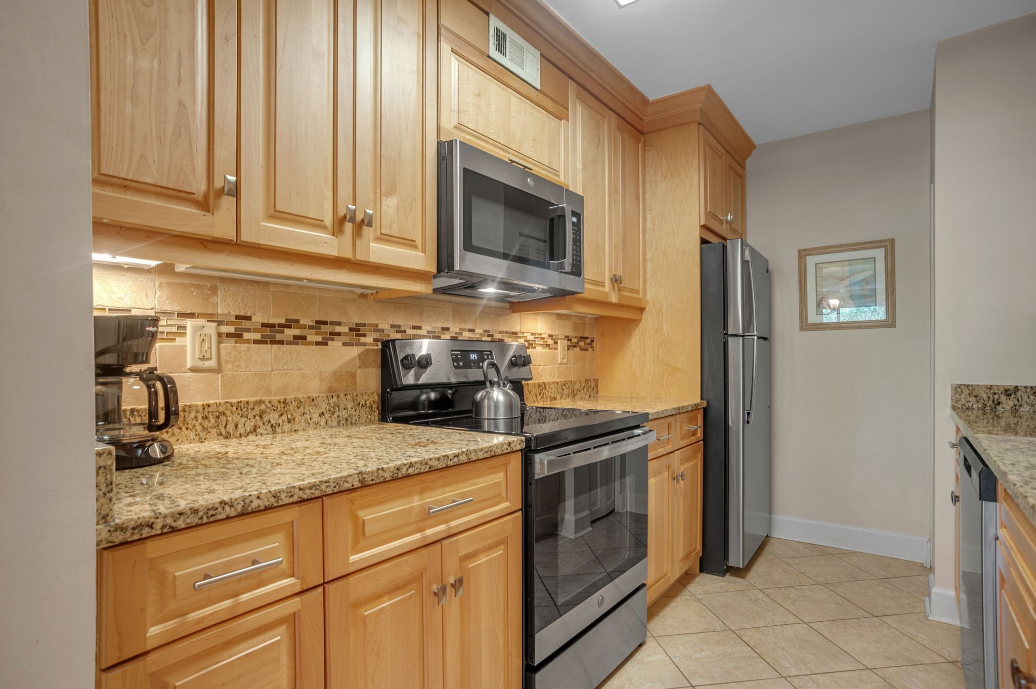 A kitchen with wooden cabinets, a stainless steel microwave, a stove, and a refrigerator.