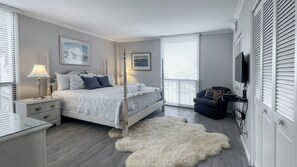 A bedroom with a bed, bedside tables, a lamp, a fluffy rug, a chair, and a TV mounted on the wall. - 1034 Caravel Court at The Sea Pines Resort (Hilton Head Island)