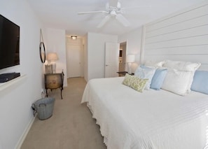 Une chambre à coucher avec un lit, un ventilateur de plafond, une télévision et une lampe.