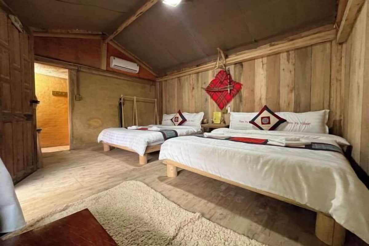 A room with two beds, wooden walls, a hanging red decoration, and a door leading to another room.