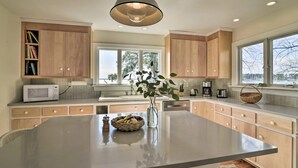 A modern kitchen with a central island, wooden cabinets, a microwave, and a large window providing natural light.