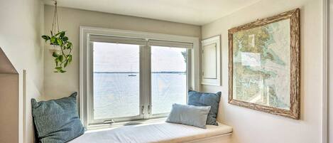 Ein Zimmer mit einer eingebauten Sitzbank an einem großen Fenster mit Blick auf ein Gewässer, einer hängenden Pflanze und einer gerahmten Karte an der Wand.