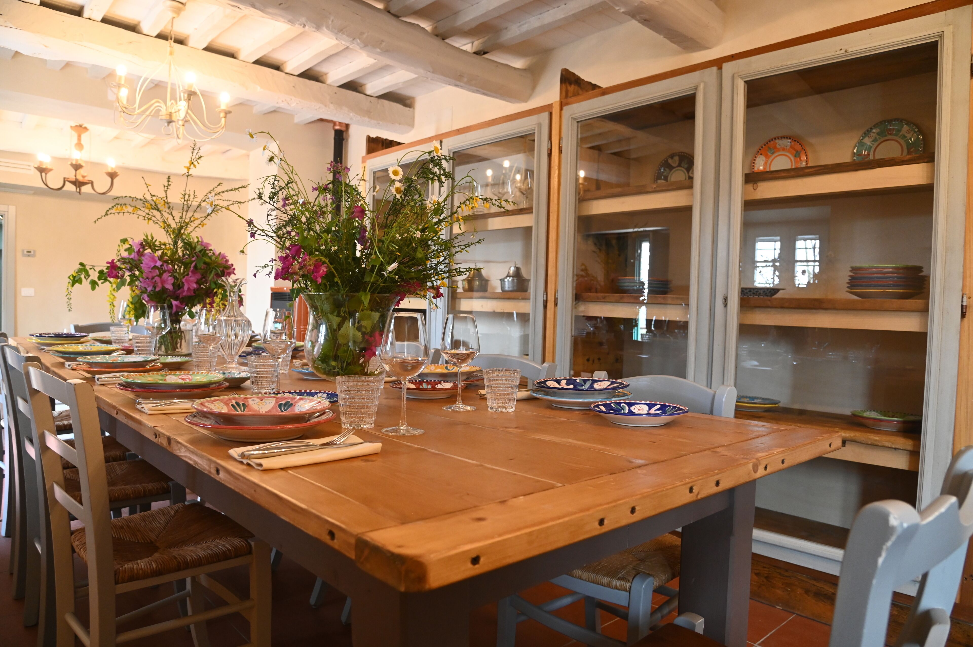 Un tavolo da pranzo in legno apparecchiato con piatti, bicchieri e un vaso di fiori.