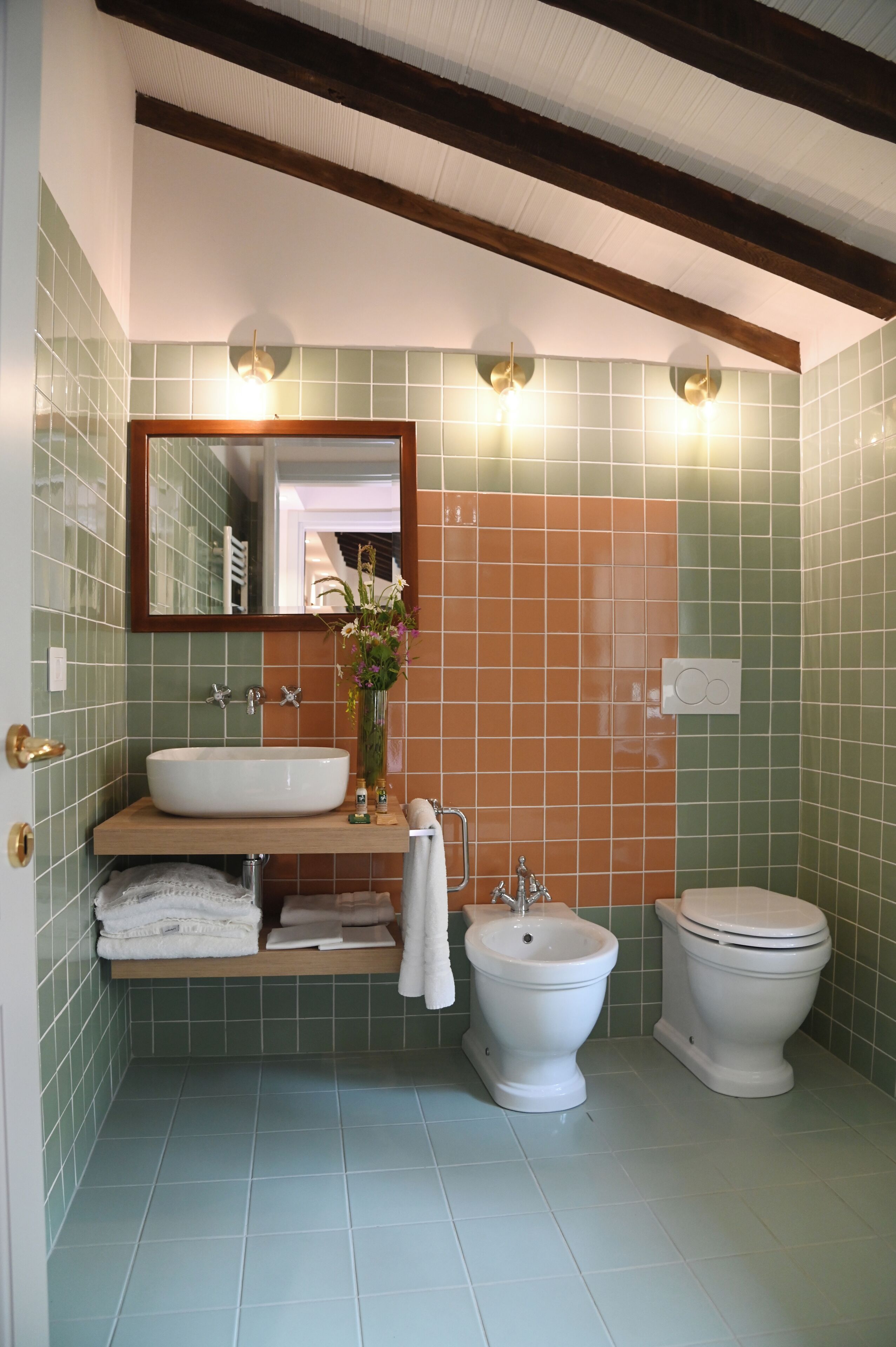 Een badkamer met een wastafel, bidet en toilet, betegeld in groen en oranje.