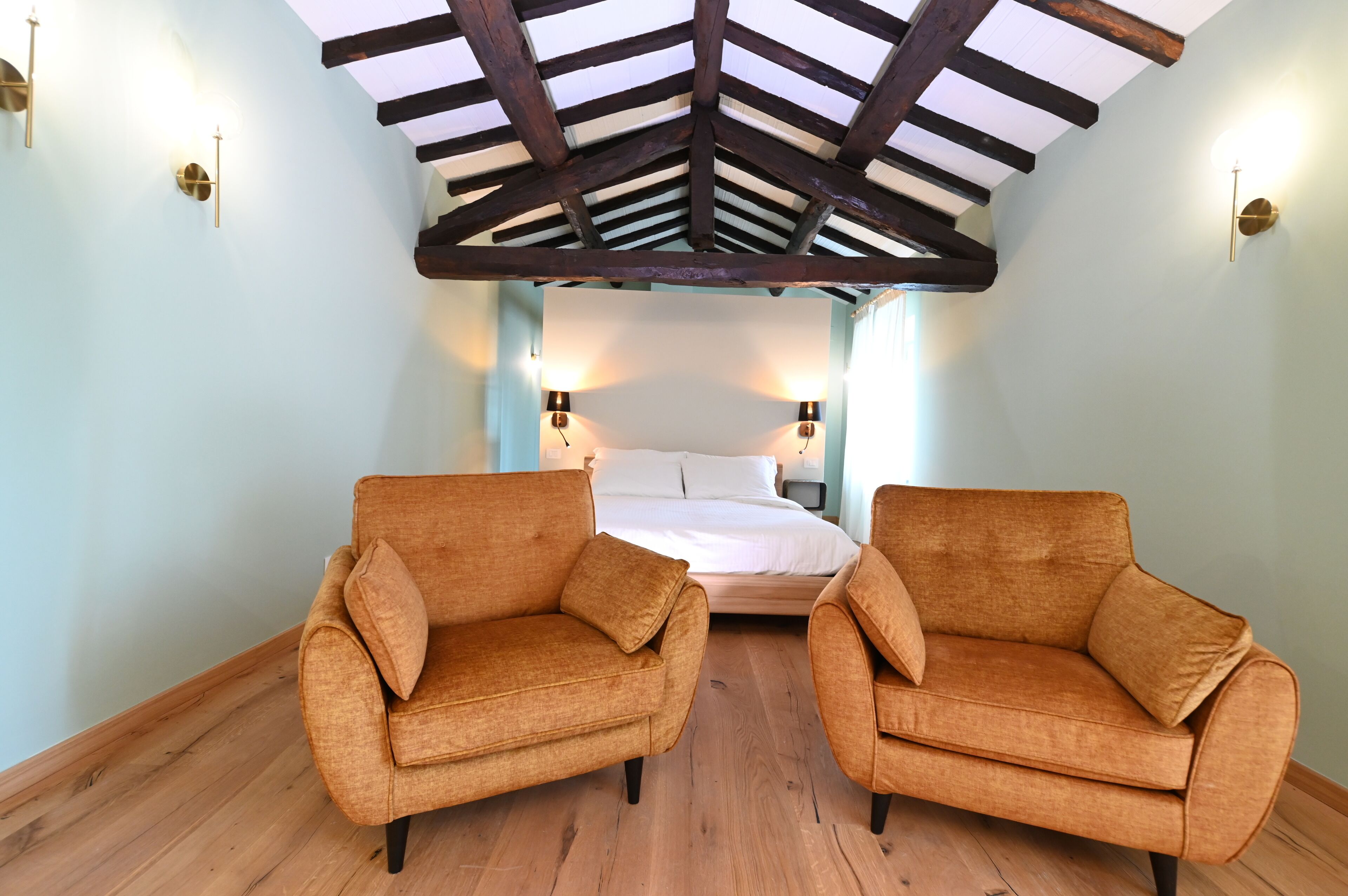 Ein Zimmer mit hohen Decken, Holzbalken, zwei Sofas, einem Bett und Wandleuchten.