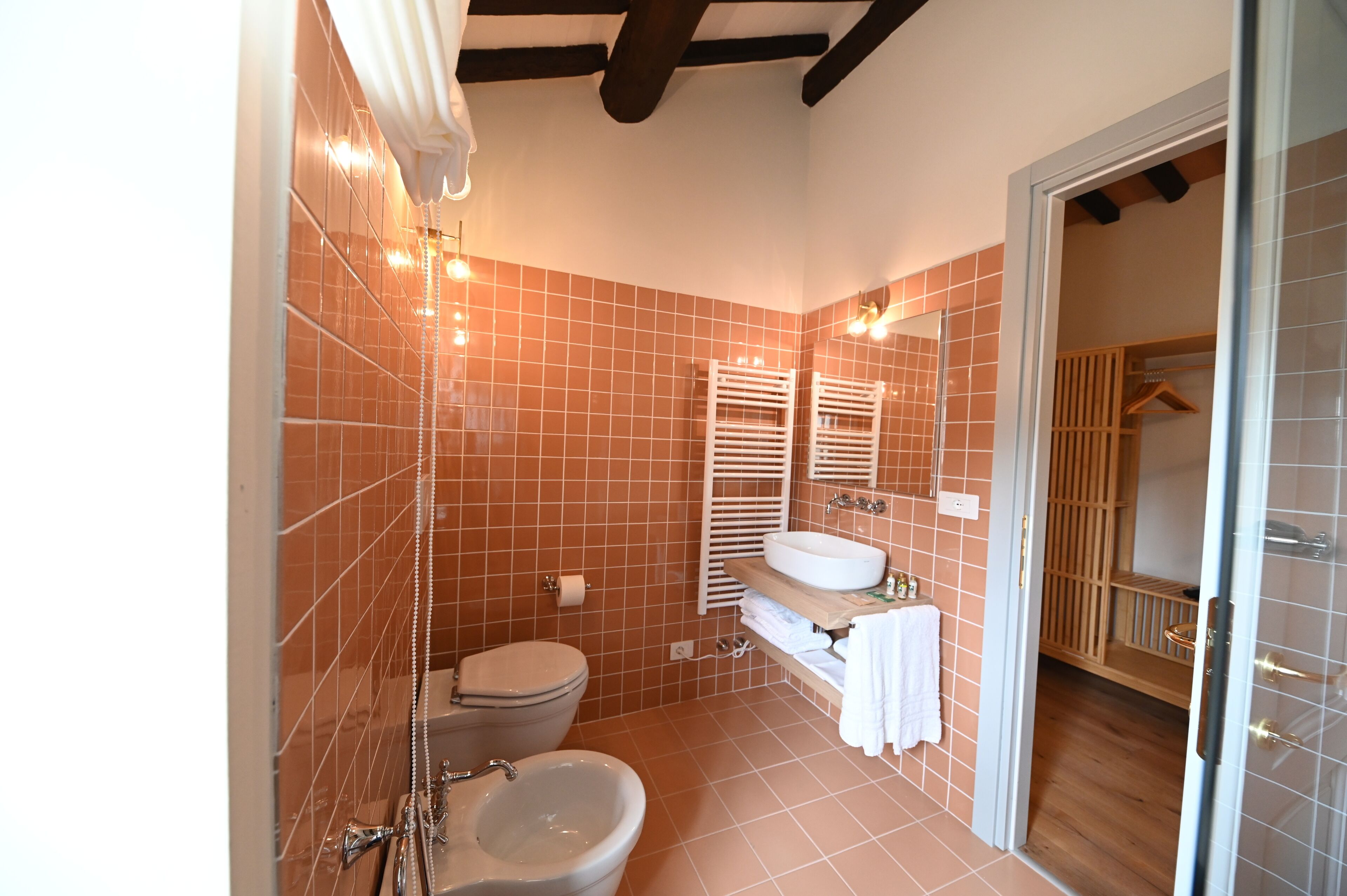Een badkamer met toilet, bidet en wastafel, betegeld in een warme kleurenschaal.