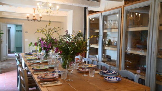 Une table à manger dressée avec des assiettes, des verres et un vase de fleurs.