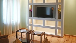 Un salon doté d’un téléviseur fixé au mur, de bibliothèques intégrées, d’un plancher en bois et d’un plafond avec des poutres apparentes.
