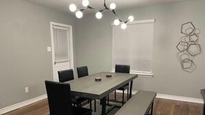 A dining area with a rectangular table, black chairs, a bench, and a modern light fixture. - Play & Relax — 4 Kings, Pool Table & 5 TVs Near JW Marriott TPC (San Antonio)
