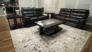 A modern living room with leather sofas, a glass coffee table, and a patterned rug. - Play & Relax — 4 Kings, Pool Table & 5 TVs Near JW Marriott TPC (San Antonio)