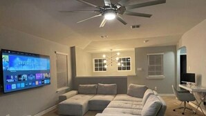 A living room with a large flat-screen TV, a ceiling fan, a pool table, and a gray sectional sofa. - Play & Relax — 4 Kings, Pool Table & 5 TVs Near JW Marriott TPC (San Antonio)