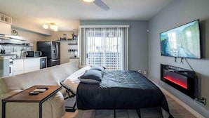Un dormitorio pequeño con cama, televisor montado en la pared, ventilador de techo y ventana con persianas.