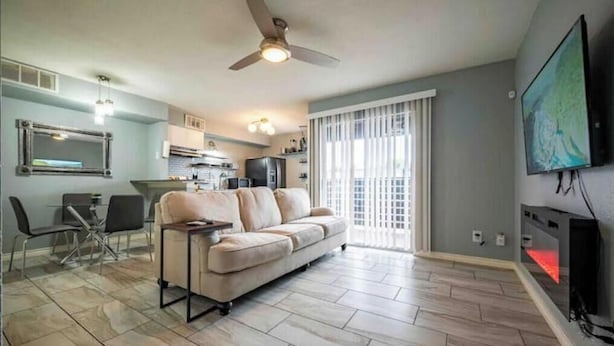 Una sala de estar con sofá, una mesa de comedor con sillas, una zona de cocina y un televisor montado en la pared.