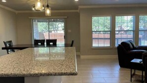 A spacious kitchen with a granite countertop, pendant lighting, and large windows offering a view of the outdoors.