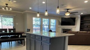 A modern kitchen with a central island, pendant lighting, and a ceiling fan.