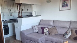 A modern living room with a grey sectional sofa, wooden dining table, and a kitchen area with white cabinets and a tiled backsplash. - Magnificent T4 sea view (Carthagène)