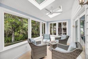 A sunroom with wicker furniture, large windows, and a ceiling fan.