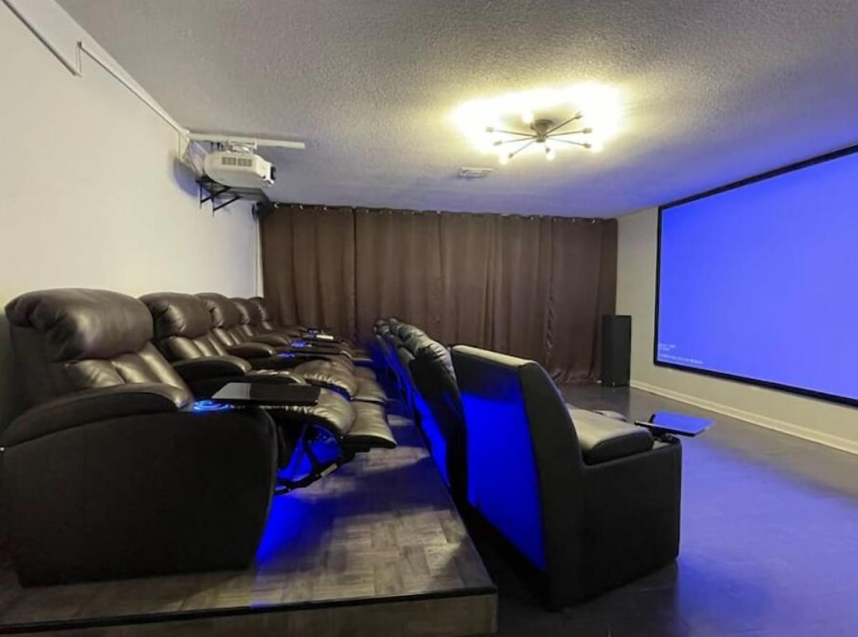 Sala de cinema doméstica com sofá reclinável, projetor no teto e tela grande.