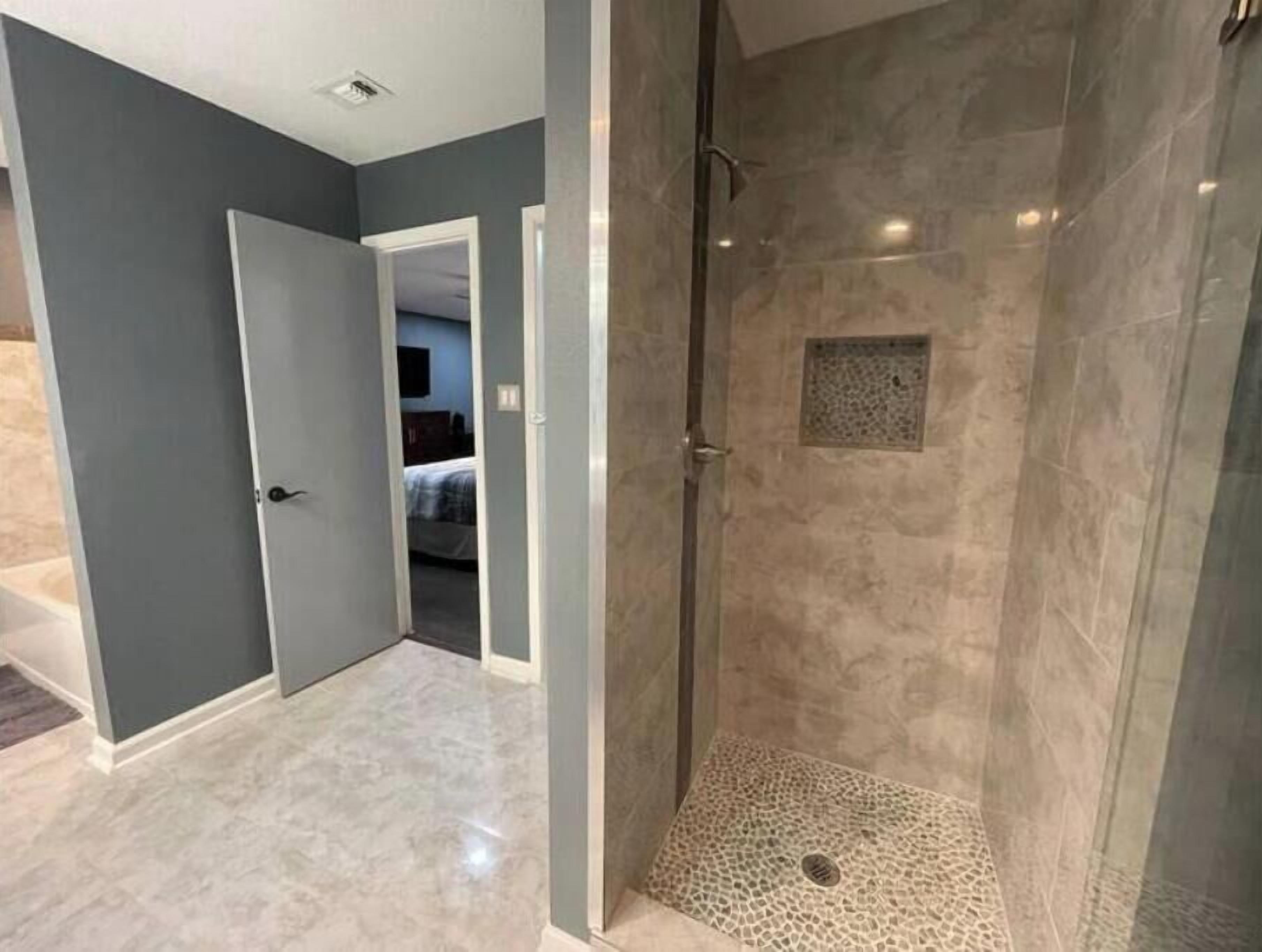 A modern bathroom with a glass-enclosed shower, marble flooring, and a visible door leading to another room.