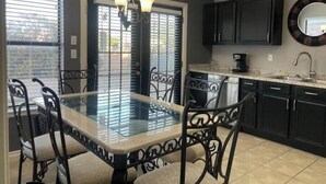 A kitchen with a glass dining table, black chairs, a coffee maker, and dark cabinets. - Spacious 5BR Longwood Home with Pool Table, Fenced Yard Near JW (San Antonio)