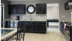 A modern kitchen with dark cabinets, a round mirror, and a dining area with a glass table and chairs. - Spacious 5BR Longwood Home with Pool Table, Fenced Yard Near JW (San Antonio)
