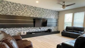 Un salon moderne avec un mur décoré d’un motif imitant la pierre, un téléviseur à écran plat et des canapés en cuir.