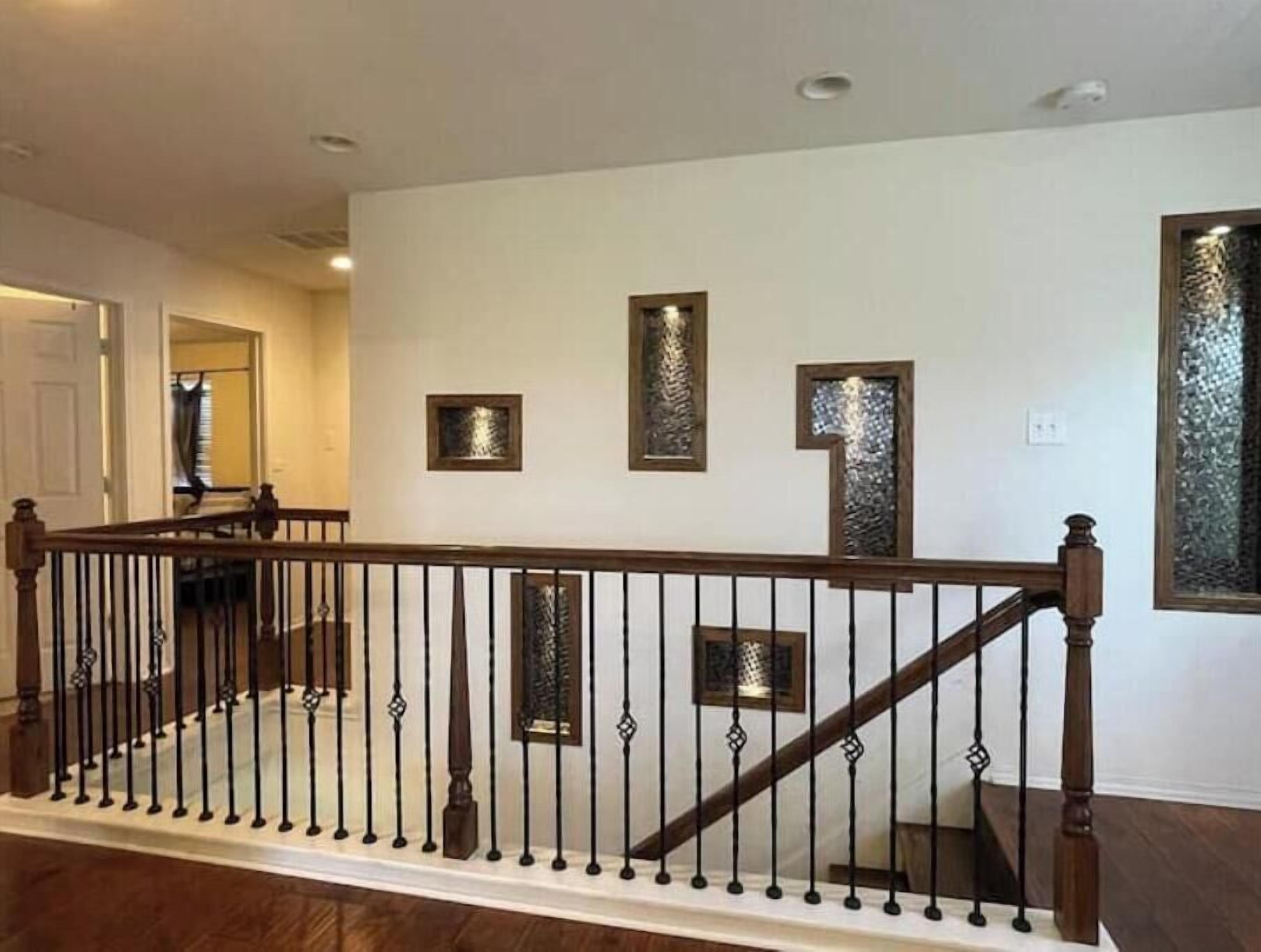 A staircase with a wooden handrail and black balusters, leading to a landing with three framed wall decorations.
