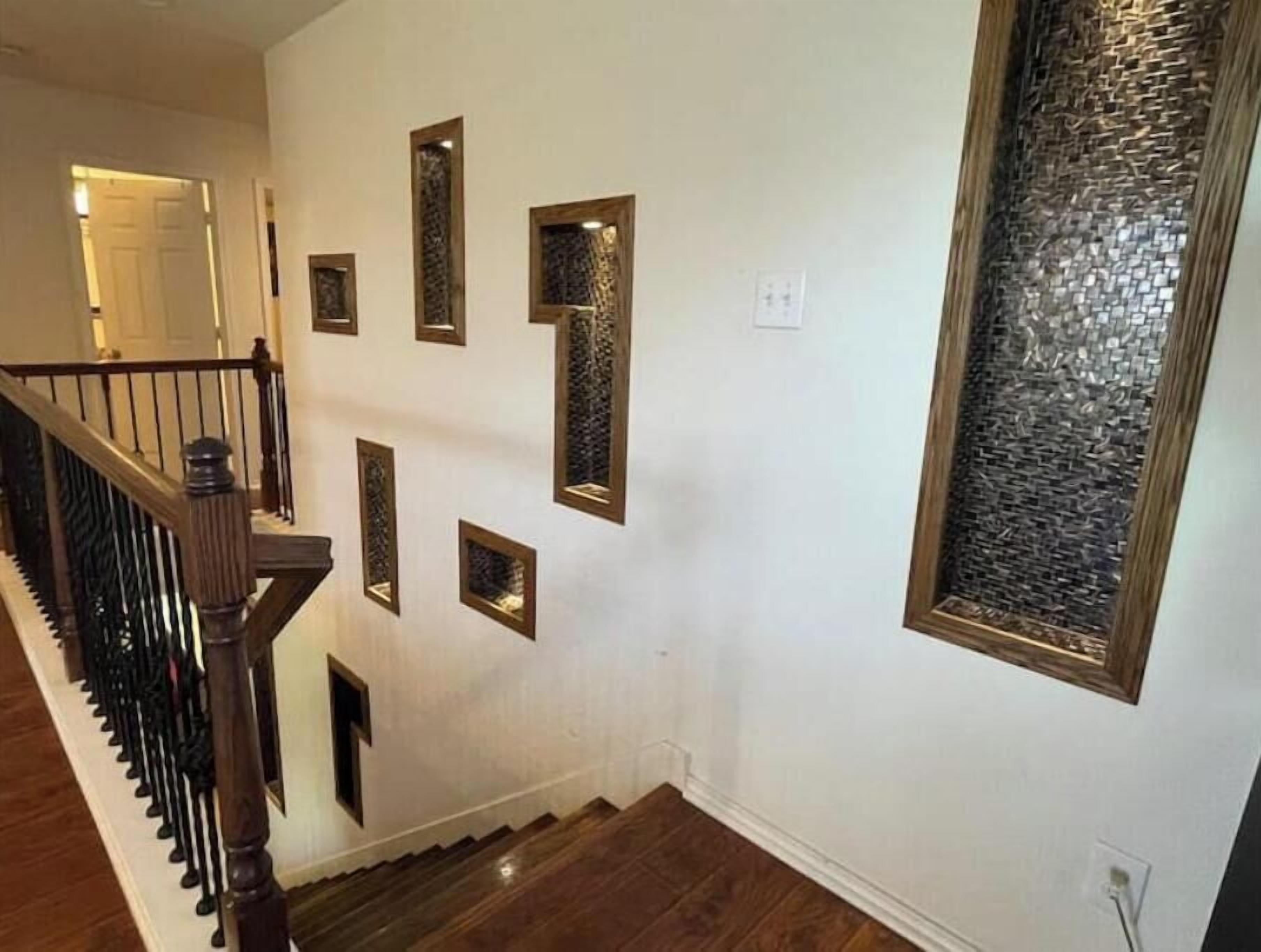 Una escalera con barandas de madera, una pared con espejos decorativos y un panel de vidrio texturizado.