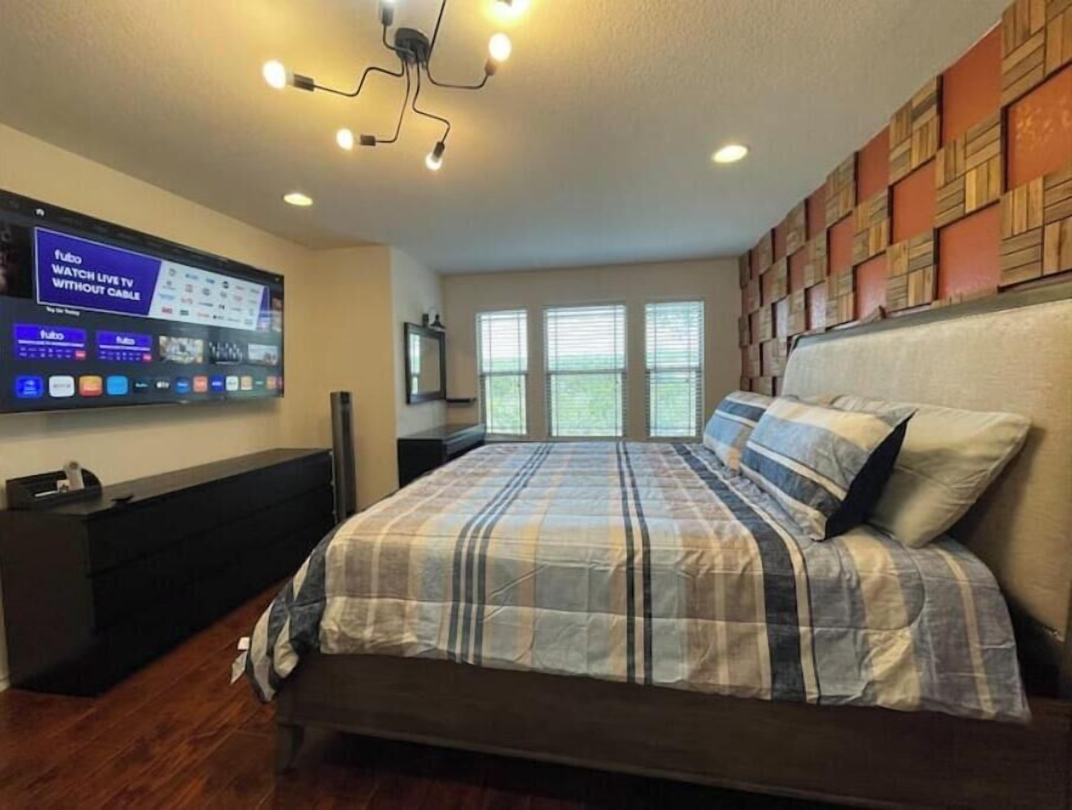 Een slaapkamer met een bed, een aan de muur bevestigde televisie en een raam met zonwering.
