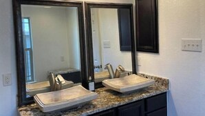 Une salle de bain avec deux lavabos, un grand miroir et un luminaire fixé au mur.